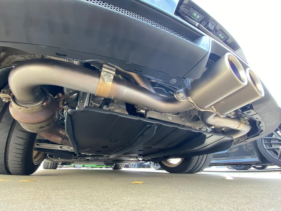 A close-up view of a performance exhaust system with dual tips and catalytic converter on a car's undercarriage.