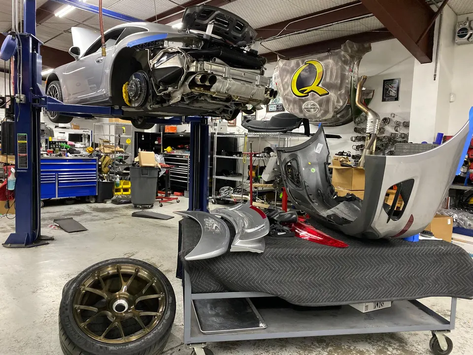 A silver Porsche 911 on a lift in a workshop with its rear bumper removed, revealing a performance exhaust system.
