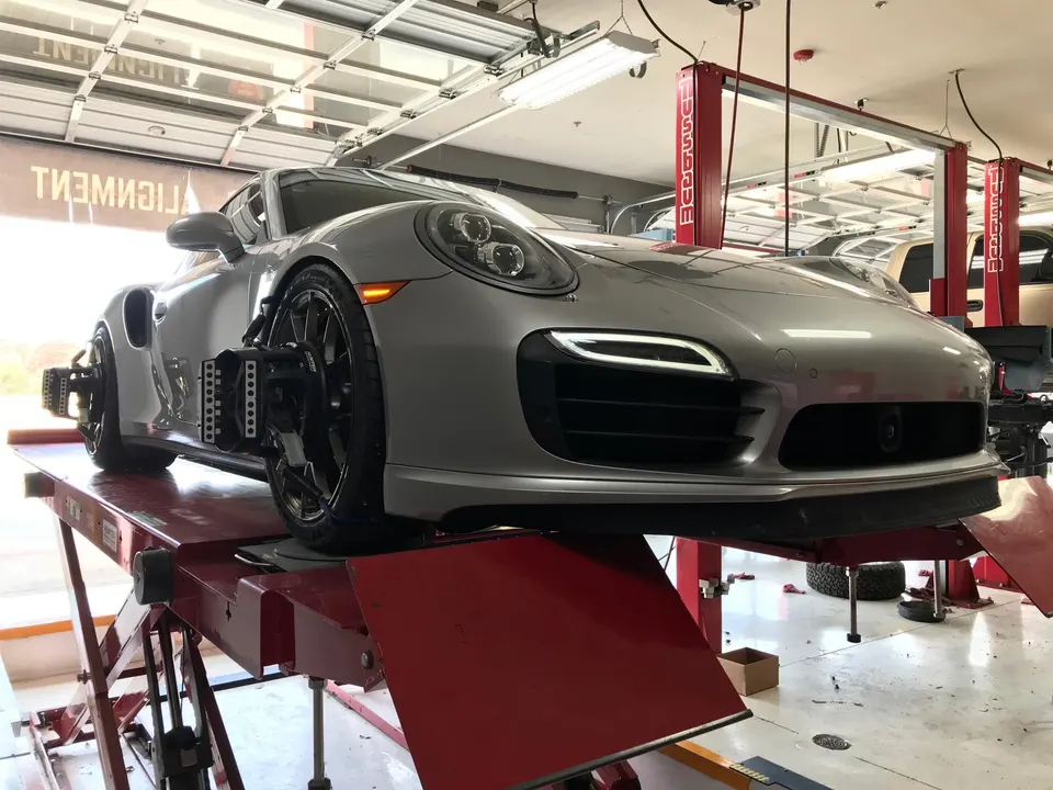 Silver Porsche 911 on an alignment rack in a performance tuning shop, with alignment sensors on the wheels.