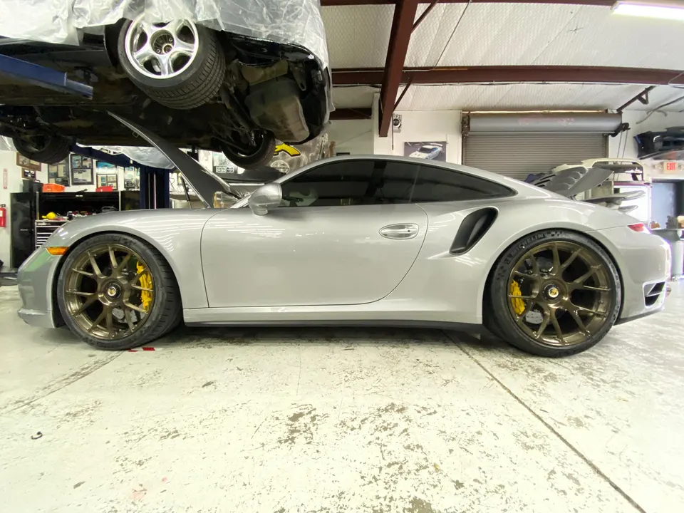 A silver Porsche 911 Turbo with bronze wheels and yellow brake calipers in a performance tuning shop.
