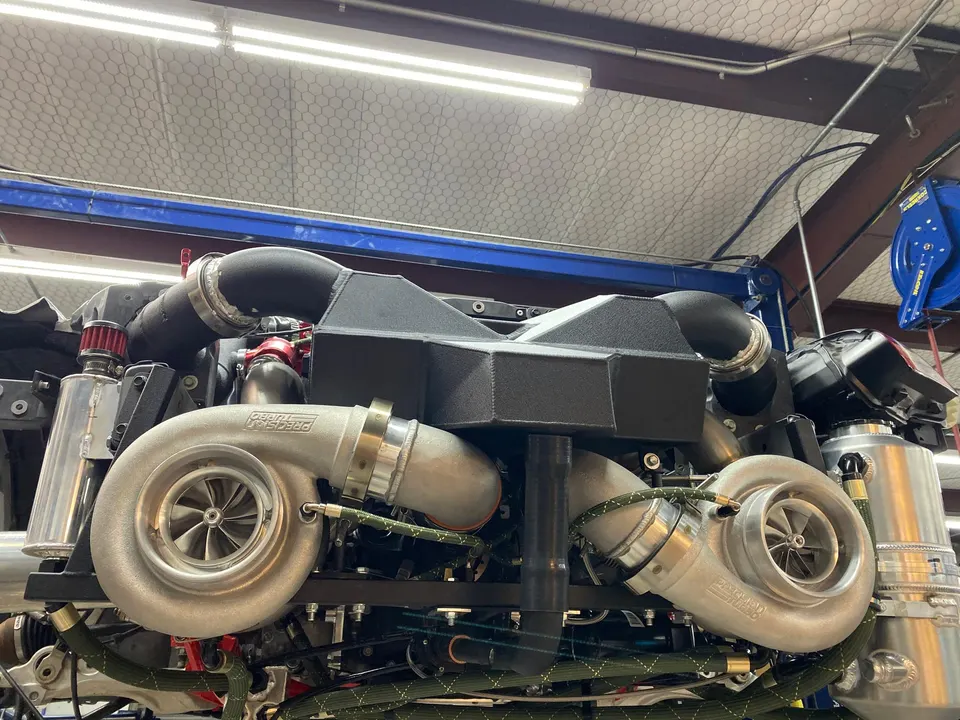 Close-up of a high-performance engine bay featuring twin Precision turbos and custom boost piping in a shop setting.