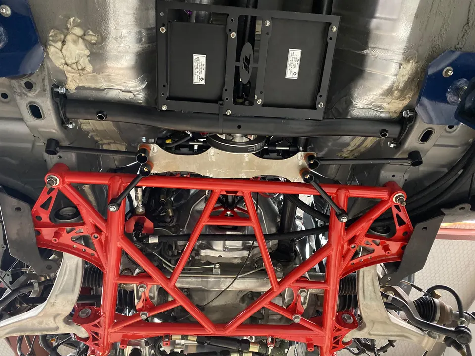 Detailed view of a car's underside, showcasing a red aftermarket subframe, suspension, and drivetrain components.