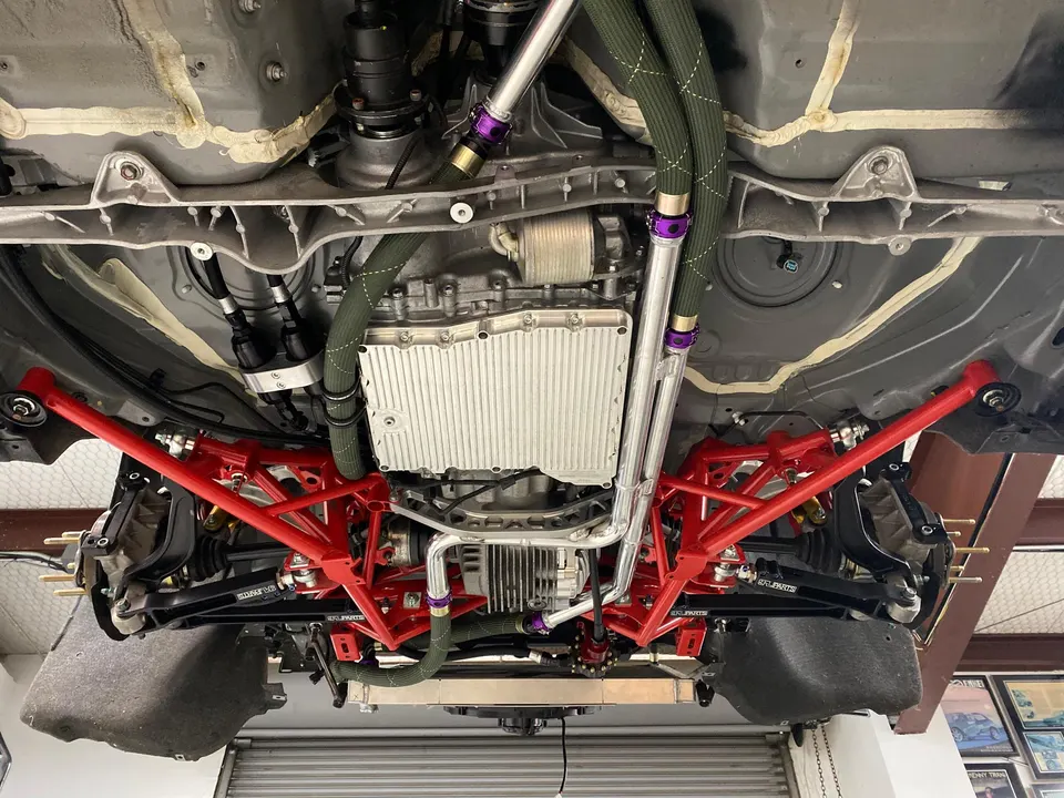 Underside view of a high-performance car on a lift, showcasing custom red suspension components and drivetrain.