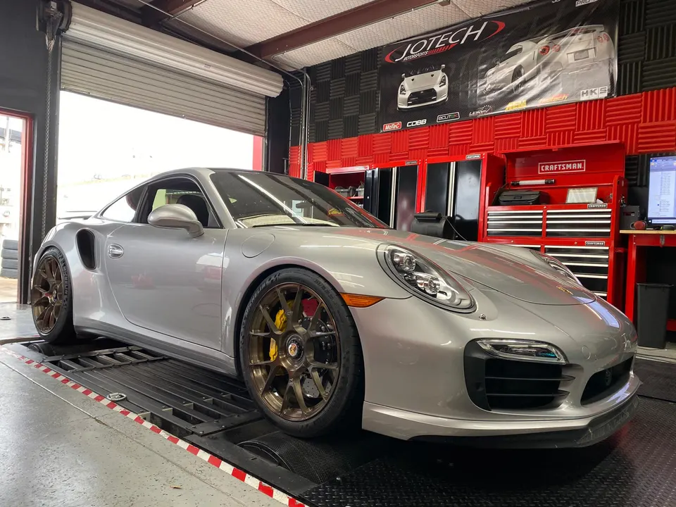 Silver Porsche 991 Turbo S on a dyno at Jotech Motorsports for performance tuning and power measurement.