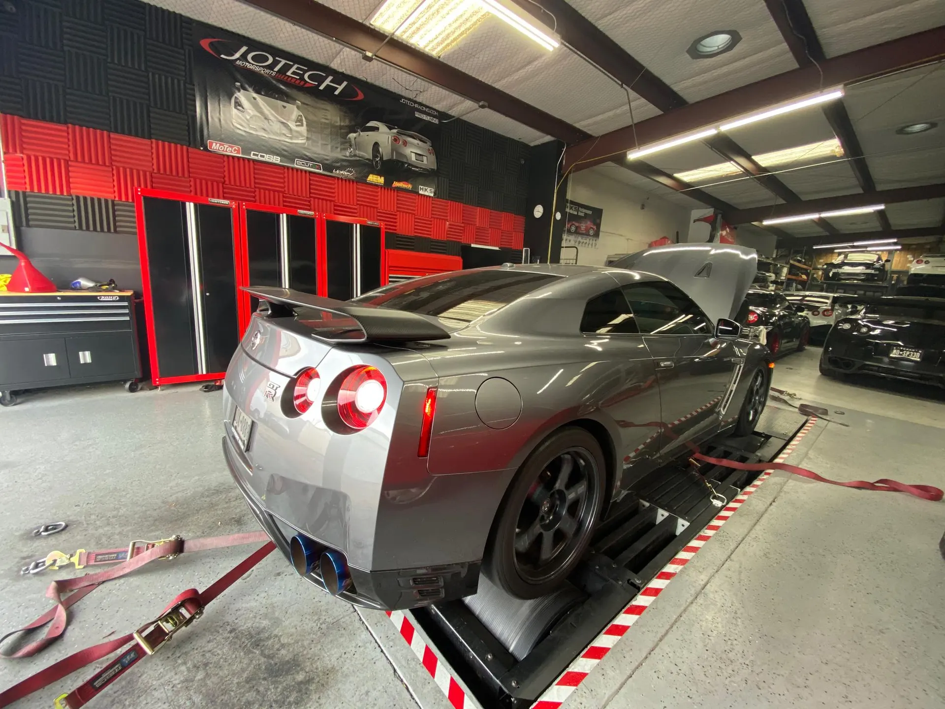 A grey Nissan GT-R strapped to a dyno at Jotech Motorsports, showcasing its aftermarket exhaust system.