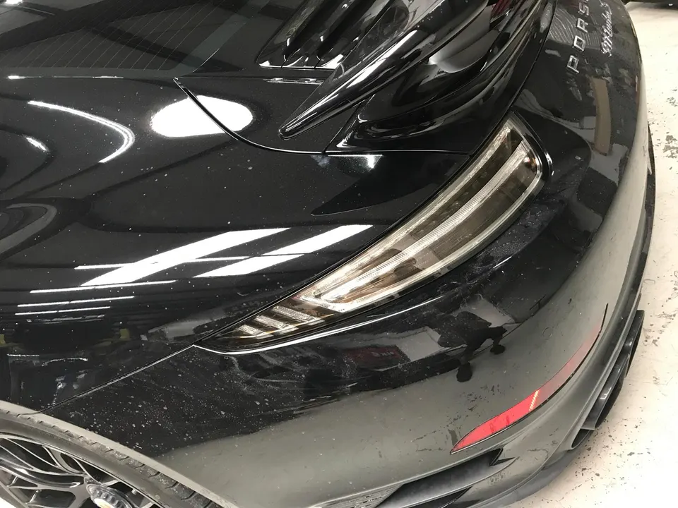 Close-up of the rear of a dirty black Porsche, showing the taillight, rear fender, and bumper.