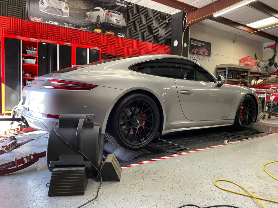 A silver Porsche 911 GTS strapped to a dynamometer in a performance tuning shop.