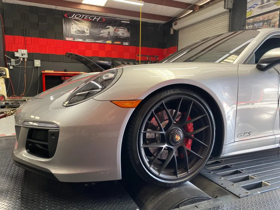 A silver Porsche 911 GTS strapped to a dynamometer at Jotech Motorsports for performance tuning.
