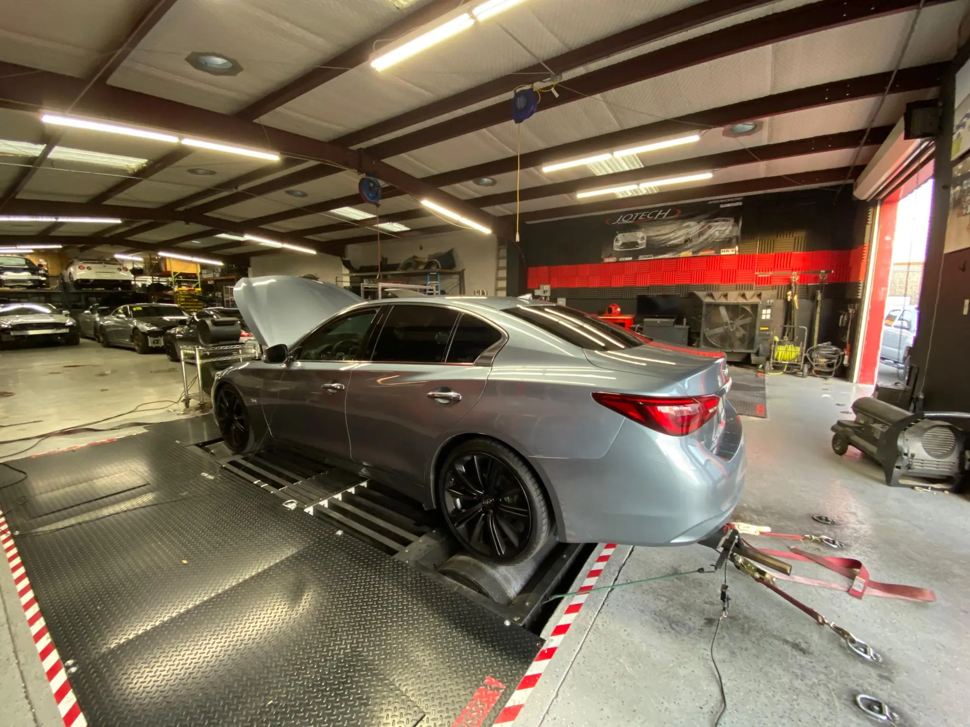 Silver Infiniti Q50 sedan strapped to a dynamometer for performance tuning at a Jotech Motorsports facility.