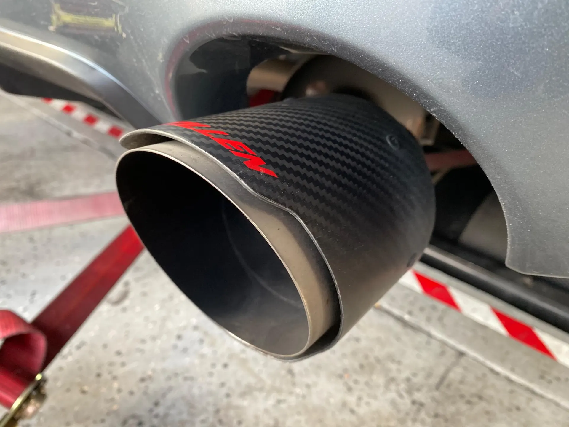 Close-up of a carbon fiber exhaust tip on a performance car, with a red dyno strap visible.