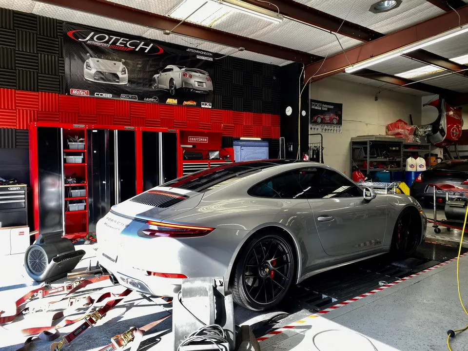 A silver Porsche 911 strapped to a dynamometer in a performance tuning shop, ready for a power run.