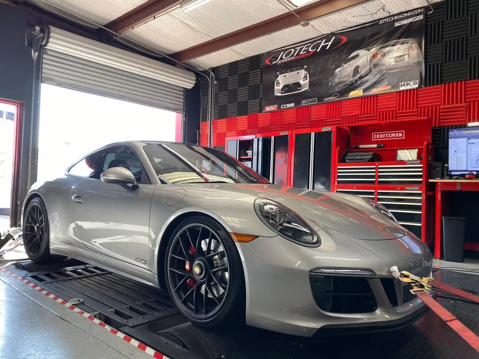 A silver Porsche 911 GTS strapped to a dyno at Jotech Motorsports for performance tuning.