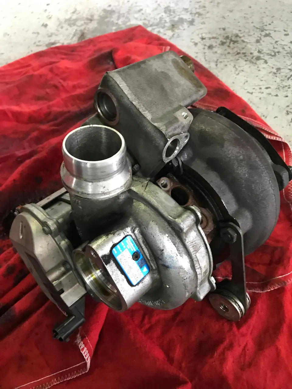 A turbocharger unit sits on a red cloth in a workshop, ready for installation or inspection.