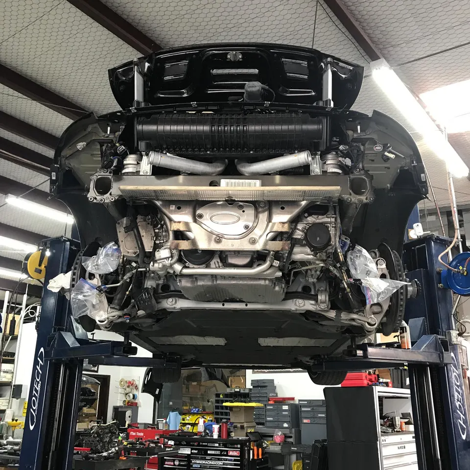 Underside of a Porsche 911 on a lift in a performance shop, showing the exhaust system and intercoolers during an upgrade.