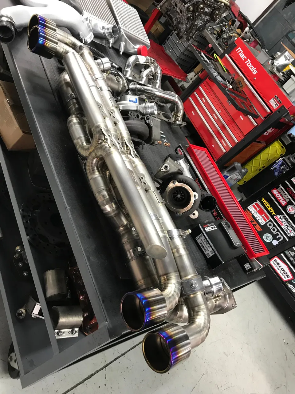 Performance exhaust system with titanium tips, intercoolers, and turbochargers laid out in a tuning shop.
