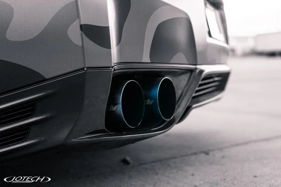 A close-up of a Nissan GT-R's rear bumper with custom exhaust tips and a camouflage wrap.