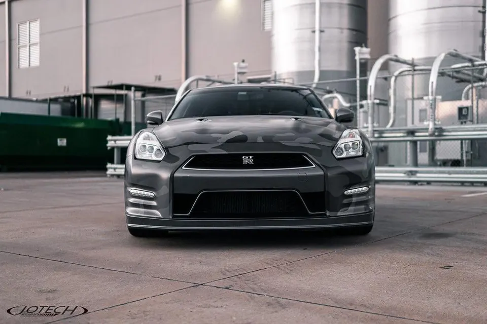 Front view of a Nissan GT-R with a grey camouflage wrap parked in an industrial setting.