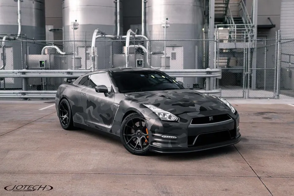 Nissan GT-R R35 with a grey camouflage wrap and aftermarket wheels parked in an industrial setting.
