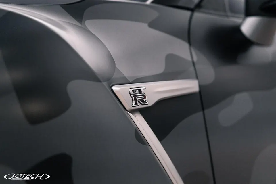 Close-up of a Nissan GT-R fender with a matte grey camouflage wrap and the GT-R badge, featuring Jotech branding.