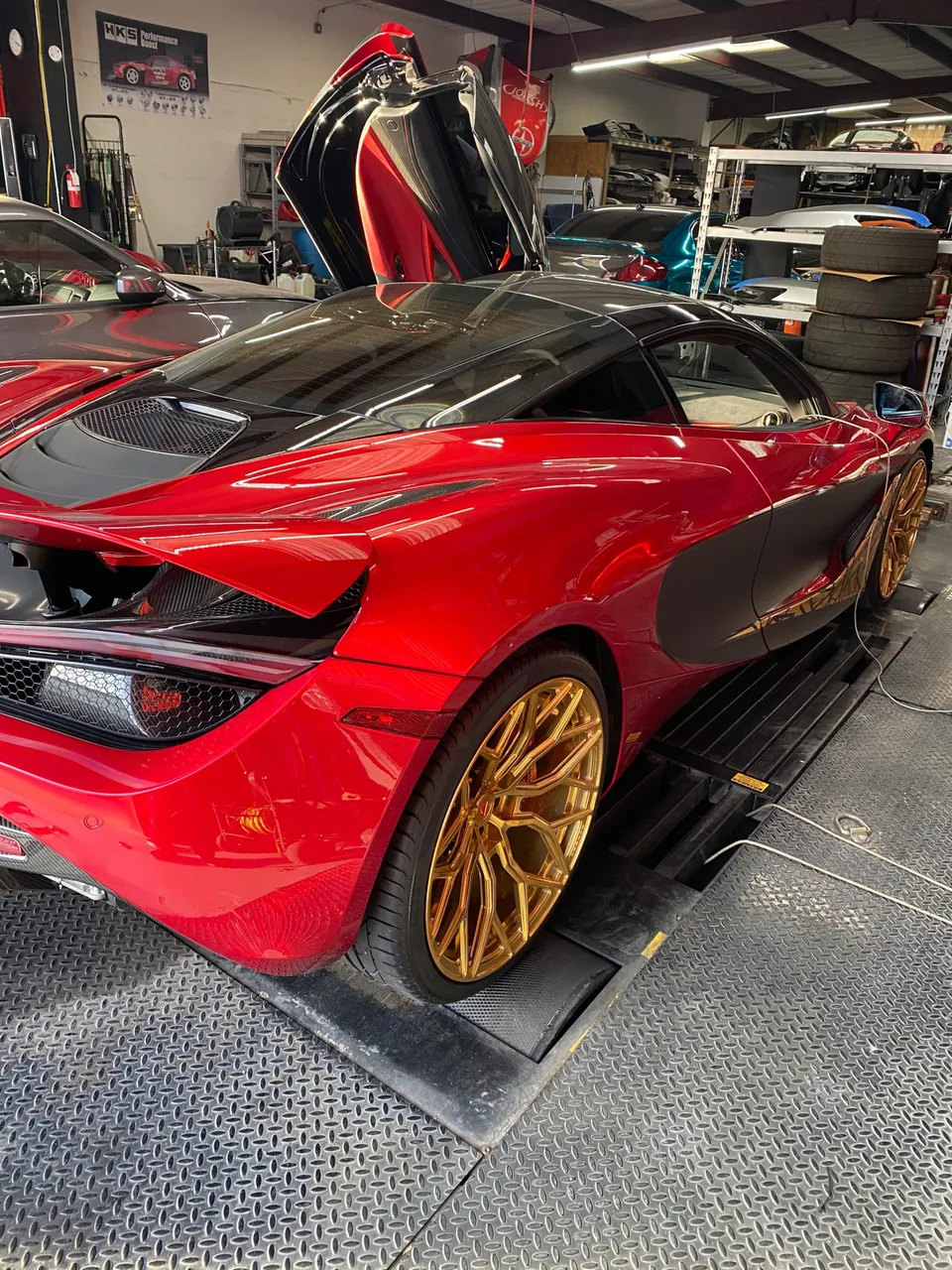 Red McLaren 720S with gold wheels on a dyno at a performance tuning shop, ready for testing.