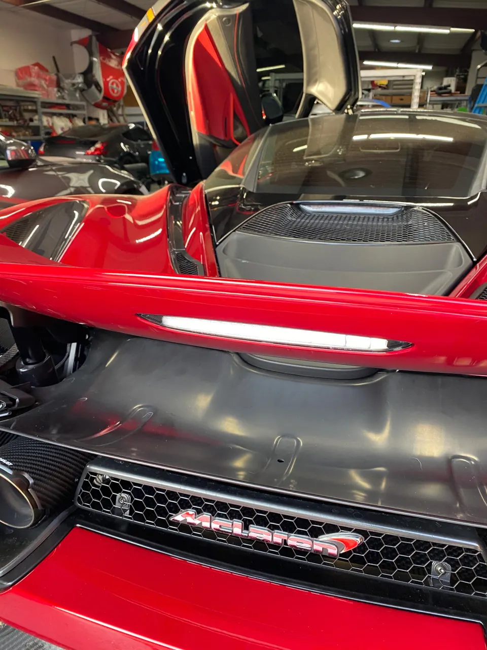 Rear view of a red McLaren in a shop, showcasing its carbon fiber exhaust and McLaren badging.