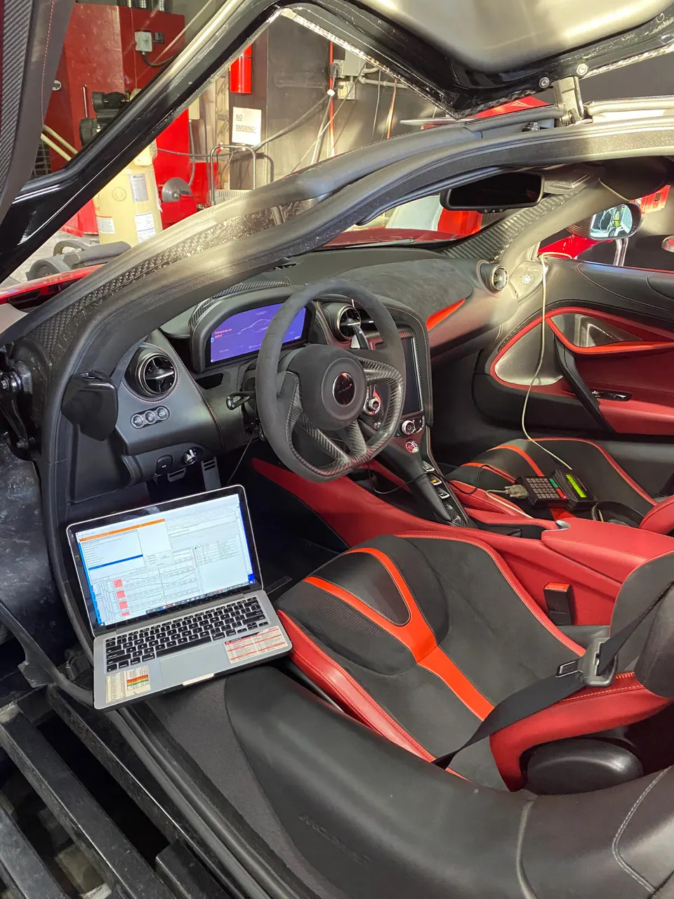 A McLaren interior with a laptop on the passenger seat, displaying tuning software in a performance shop.