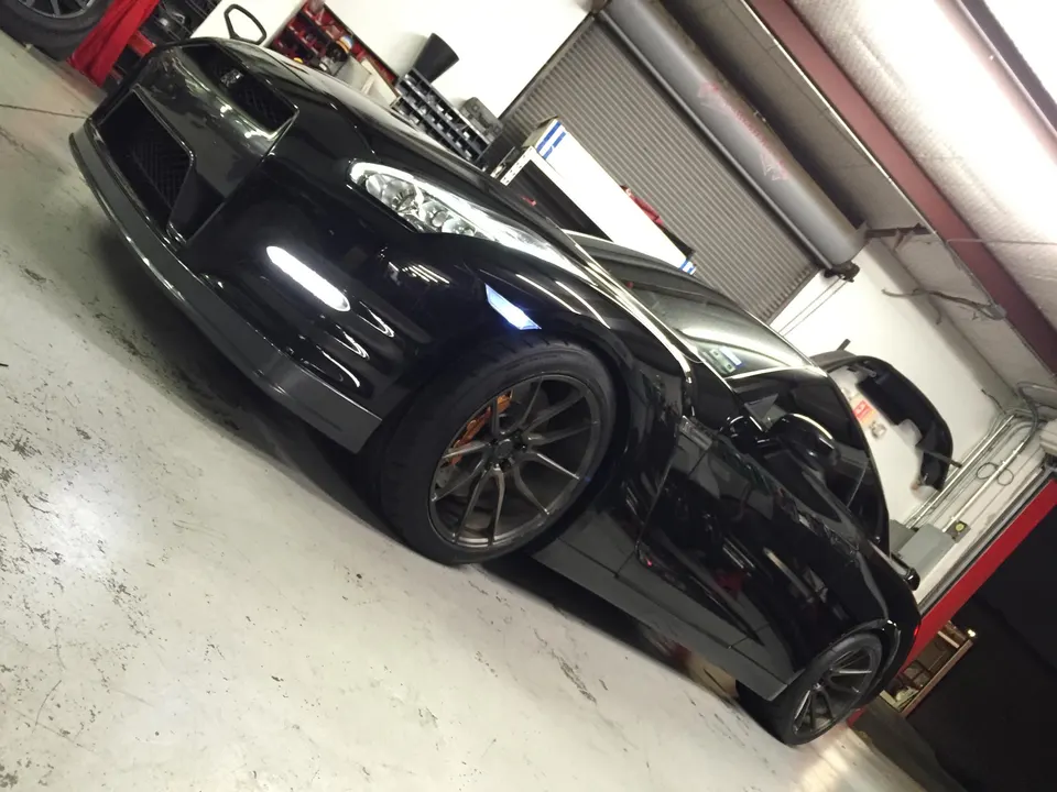 A black Nissan GT-R with aftermarket wheels and a front splitter parked in a garage.