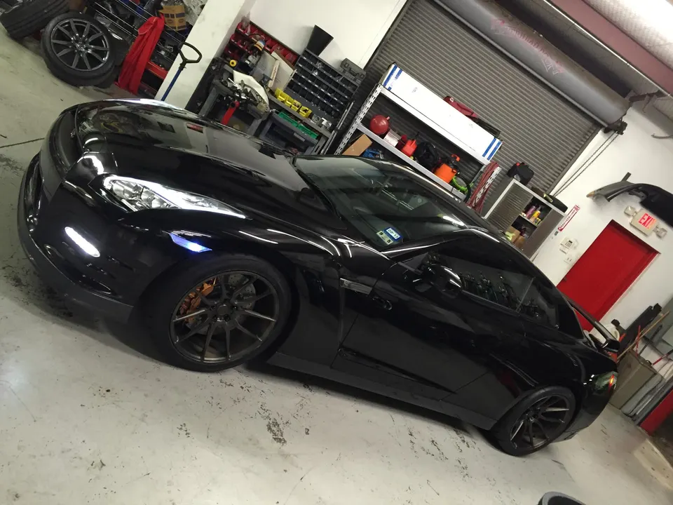 A sleek black Nissan GT-R with custom wheels and orange brake calipers parked in a well-lit performance shop.