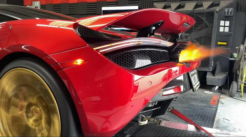 Red McLaren on a dyno with flames shooting from its exhaust during a performance test, showcasing gold wheels.