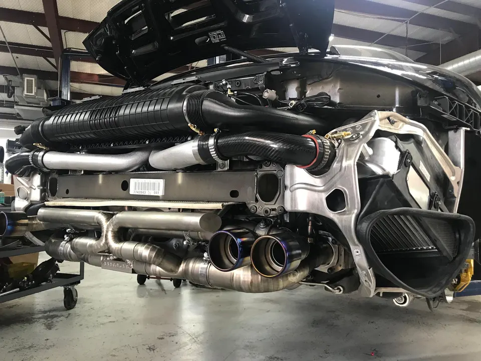 Detailed view of a McLaren's rear engine bay with a custom titanium exhaust system and turbo piping in a performance shop.