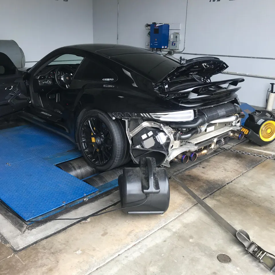 A black Porsche 911 on a dynamometer with its rear bumper removed, showcasing an aftermarket exhaust system.