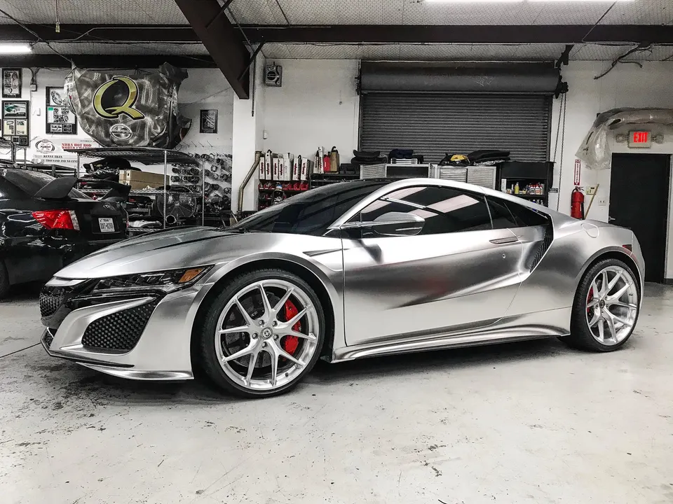 A silver wrapped Acura NSX with custom wheels and red brake calipers parked inside a performance tuning shop.