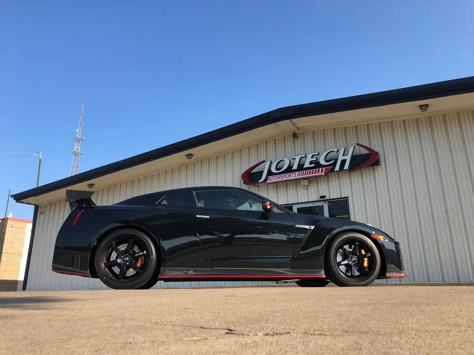 Black Nissan GT-R with aftermarket wheels and rear wing parked outside Jotech Motorsports performance shop.
