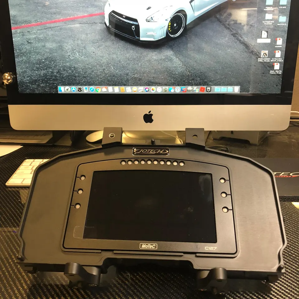MoTeC C127 digital dash unit in a Jotech housing on a carbon fiber desk, with an Apple iMac displaying a Nissan GT-R