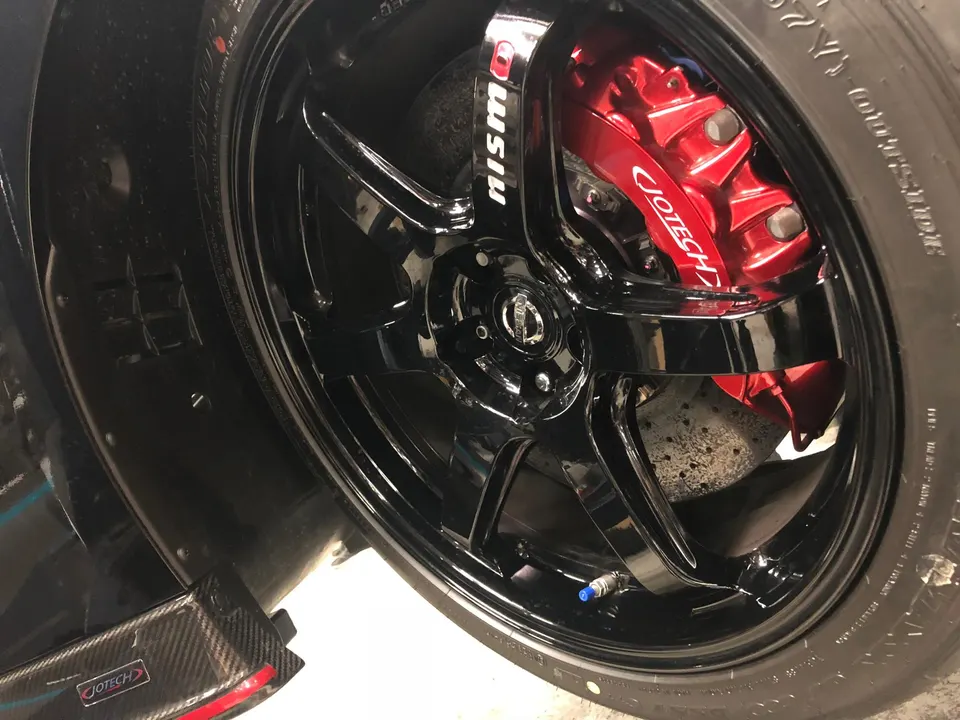 Close-up of a black Nismo wheel with red Jotech brake calipers and carbon fiber trim on a performance car.