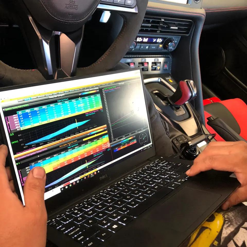 A person tuning a Nissan GT-R's engine using a laptop with specialized software, showing ignition timing and engine speed maps.