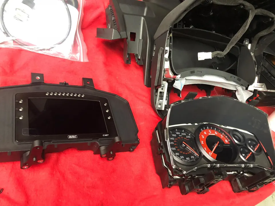 MoTeC C127 digital dash and OEM instrument cluster for a Nissan GT-R on a workbench during an electronics upgrade.