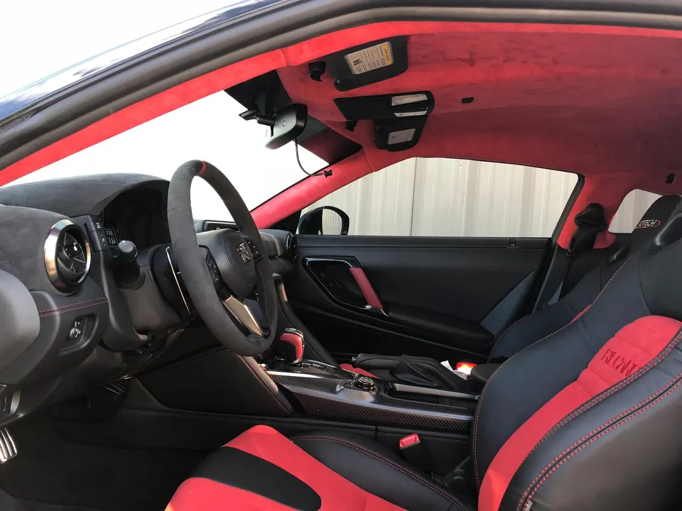 Custom red and black interior of a Nissan GT-R with aftermarket steering wheel and racing seats.