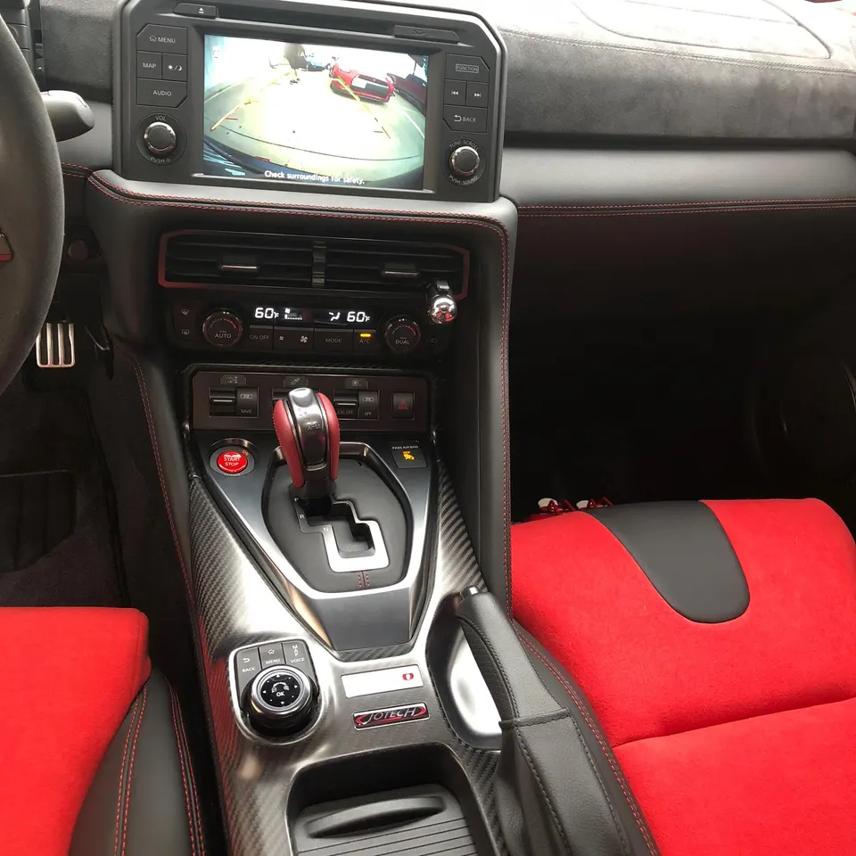 Nissan GT-R interior with red and black seats, carbon fiber trim, and infotainment screen displaying a backup camera view.