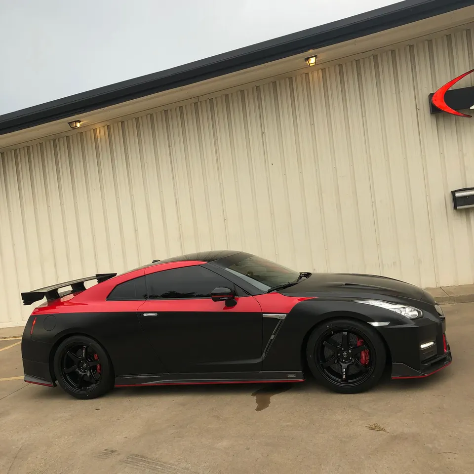 Side profile of a black and red two-tone Nissan GT-R R35 with aftermarket wheels and a large rear wing parked outside.