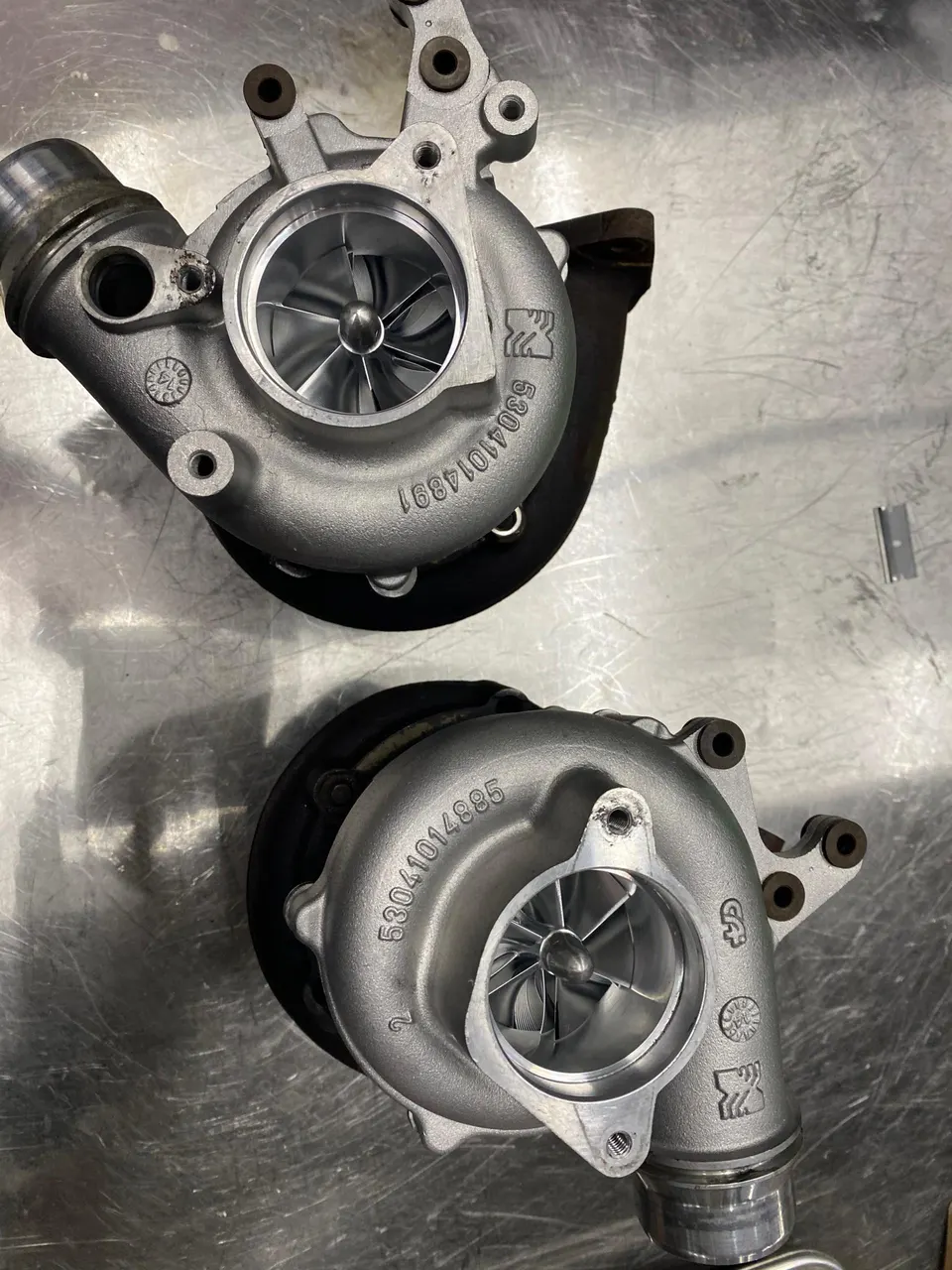 Two new turbochargers with visible compressor wheels on a metal workbench in a performance shop.