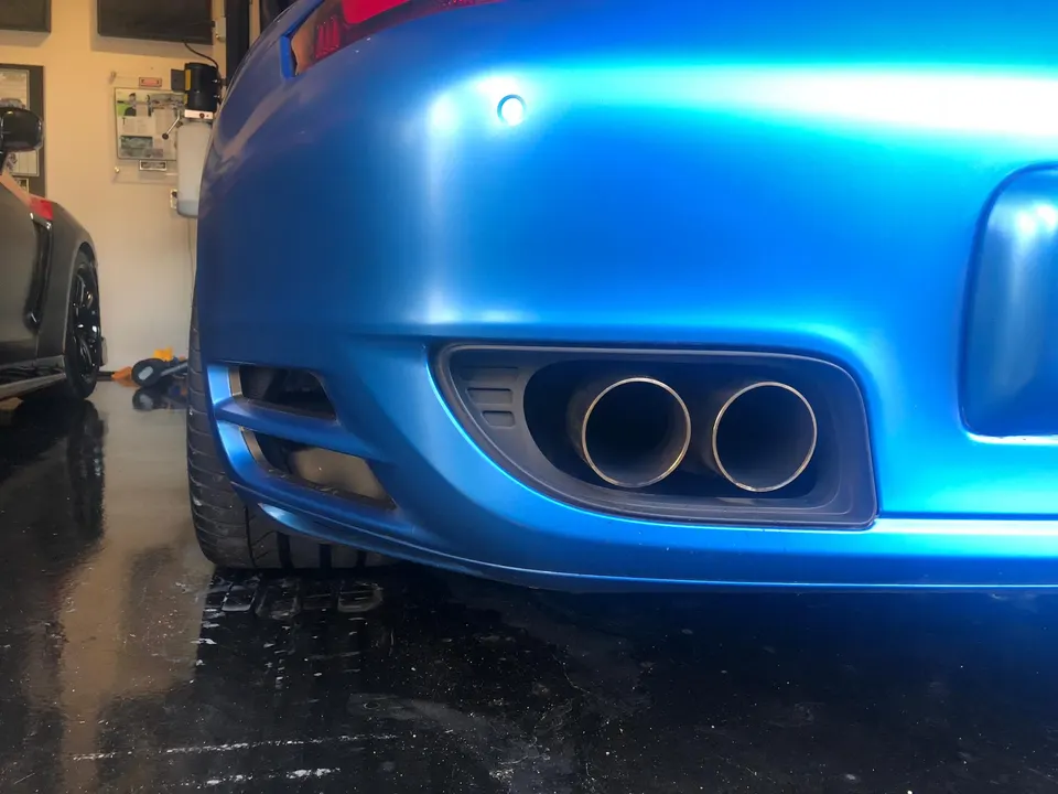 Rear view of a matte blue Porsche with dual exhaust tips in a garage.