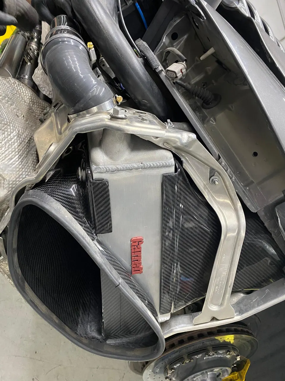 Close-up of a carbon fiber air intake system and Garrett intercooler being installed in a performance car's engine bay.
