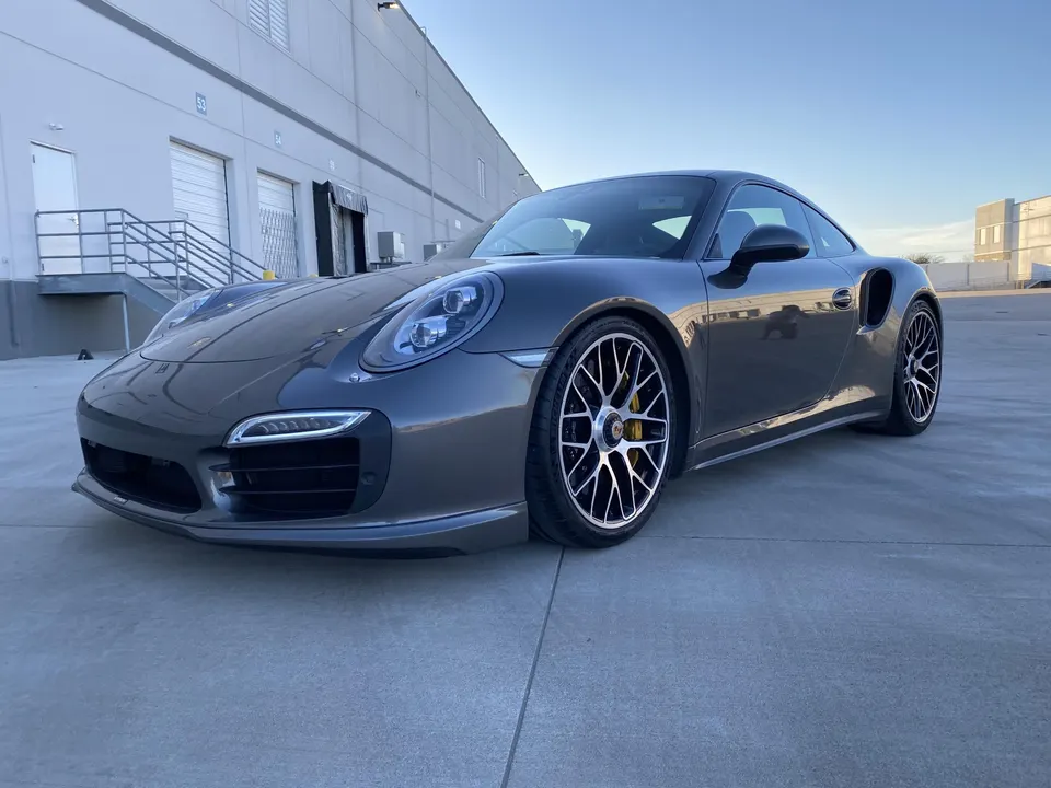 Grey Porsche 911 parked in front of a warehouse building under a clear sky.