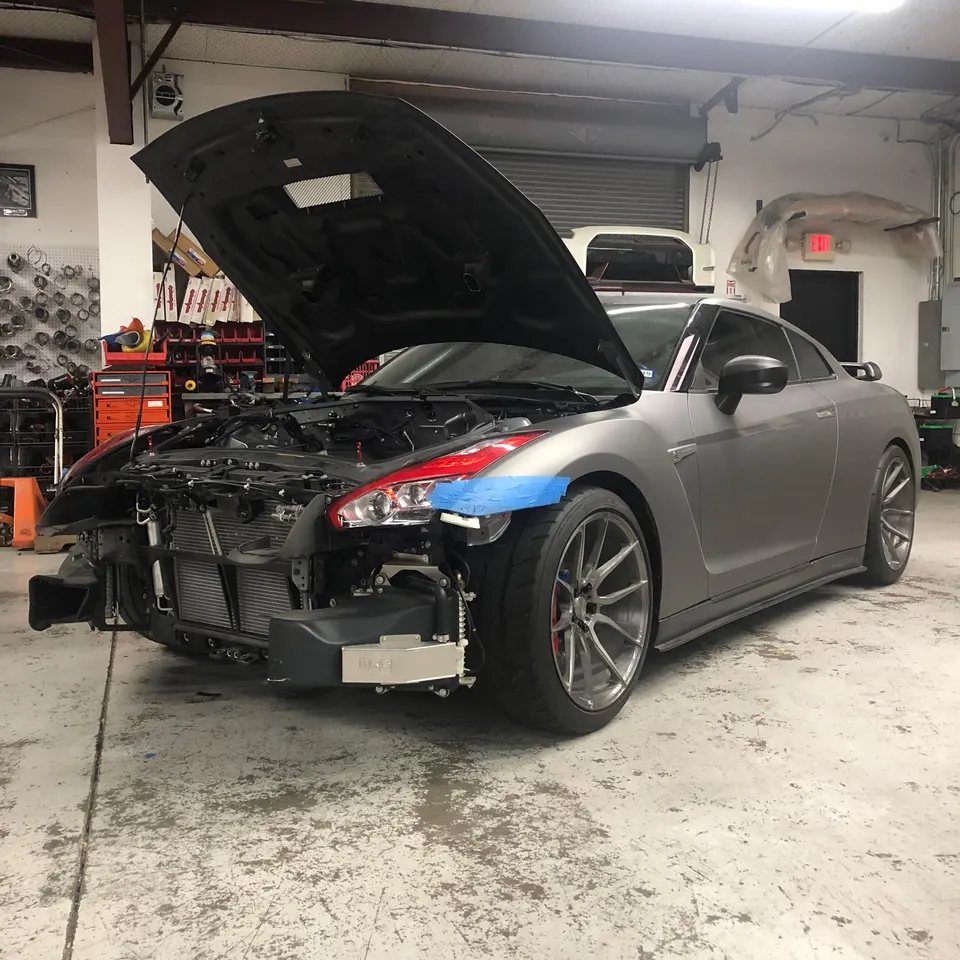 Nissan GT-R R35 in a performance shop with the front bumper removed and hood open, revealing the intercooler and engine bay.