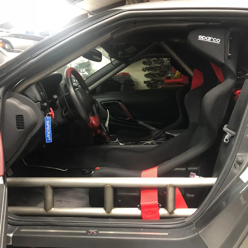 Nissan GT-R interior with Sparco racing seat, Safecraft keychain, and custom roll cage in a shop.