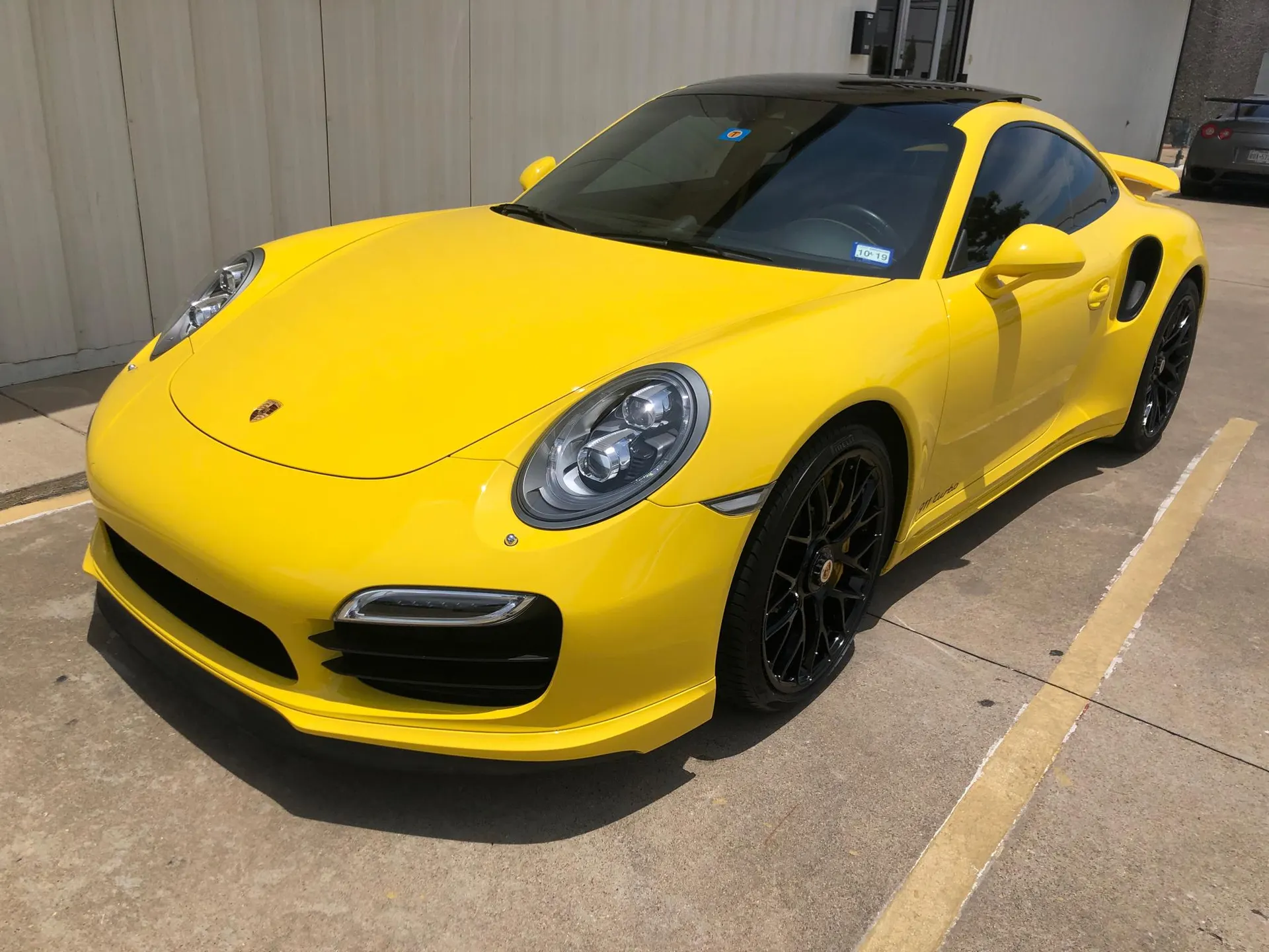 Yellow Porsche 911 Turbo S with black wheels and a front lip parked outdoors on a sunny day