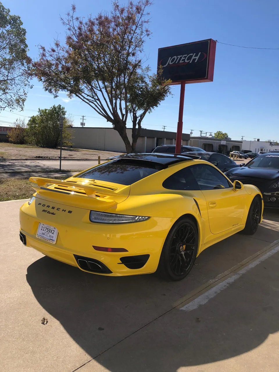 Yellow Porsche 911 Turbo parked outside Jotech Motorsports performance tuning shop on a sunny day