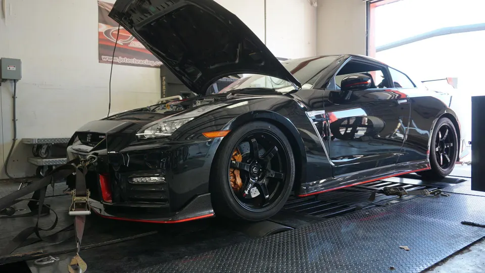 A black Nissan GT-R with its hood open strapped to a dyno at Jotech Racing for performance tuning.