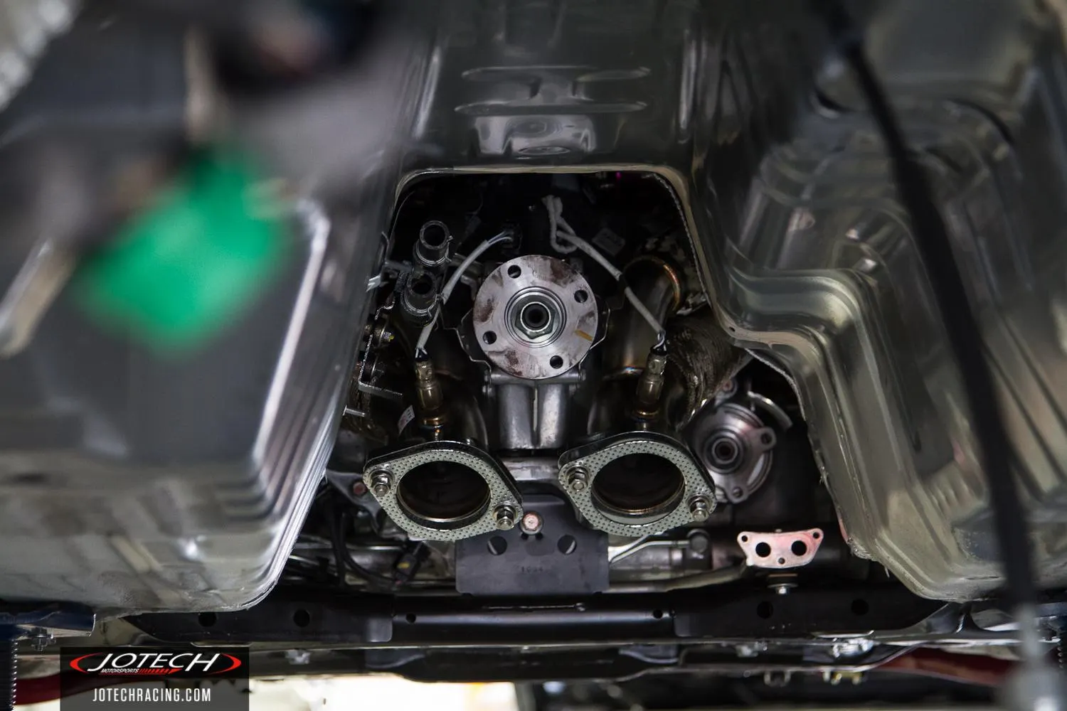 Detailed view of a car's underside, showcasing exhaust system flanges, O2 sensors, and drivetrain components.